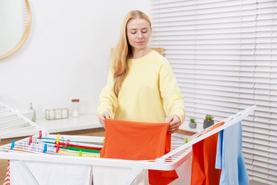 Photo of Beautiful woman hanging fresh clean laundry on drying rack at home