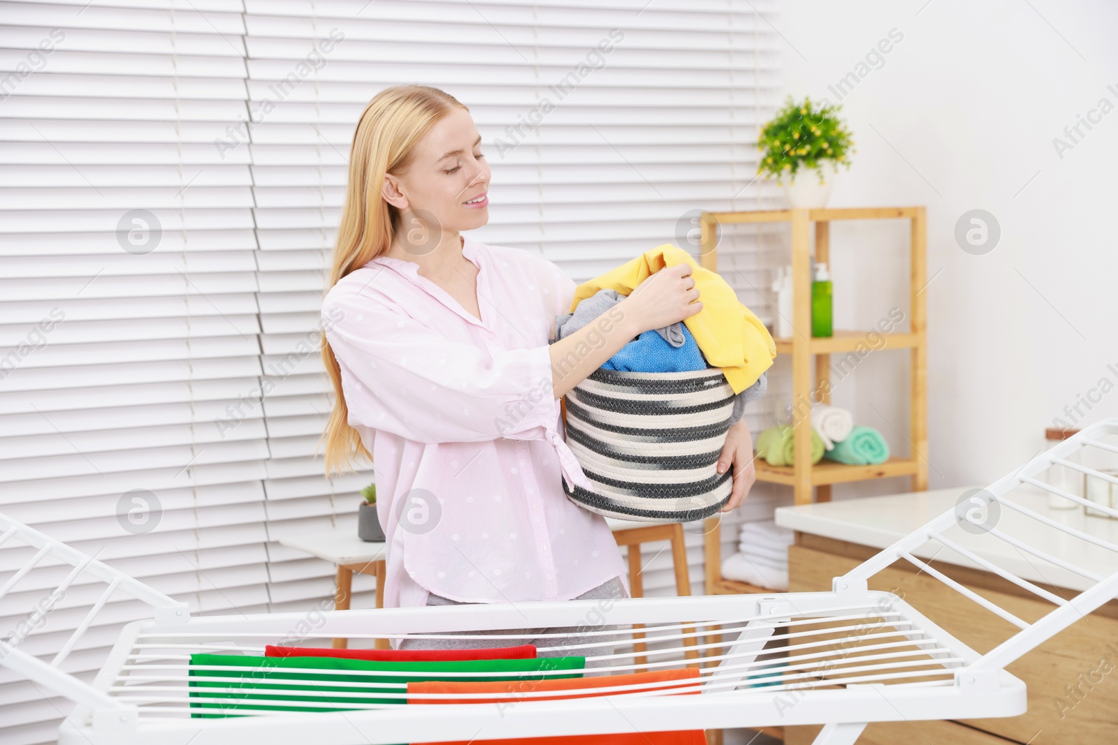 Photo of Beautiful woman hanging fresh clean laundry on drying rack at home