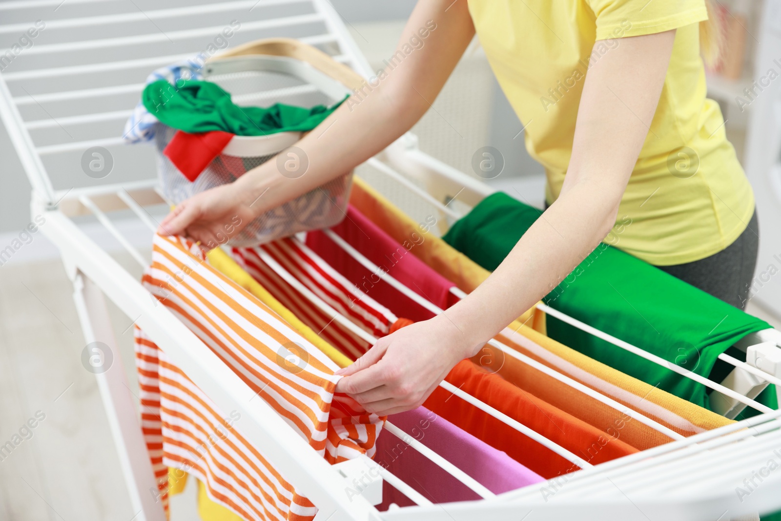 Photo of Woman hanging fresh clean laundry on drying rack at home, closeup