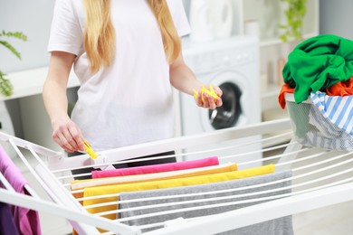 Photo of Woman hanging fresh clean laundry on drying rack at home, closeup