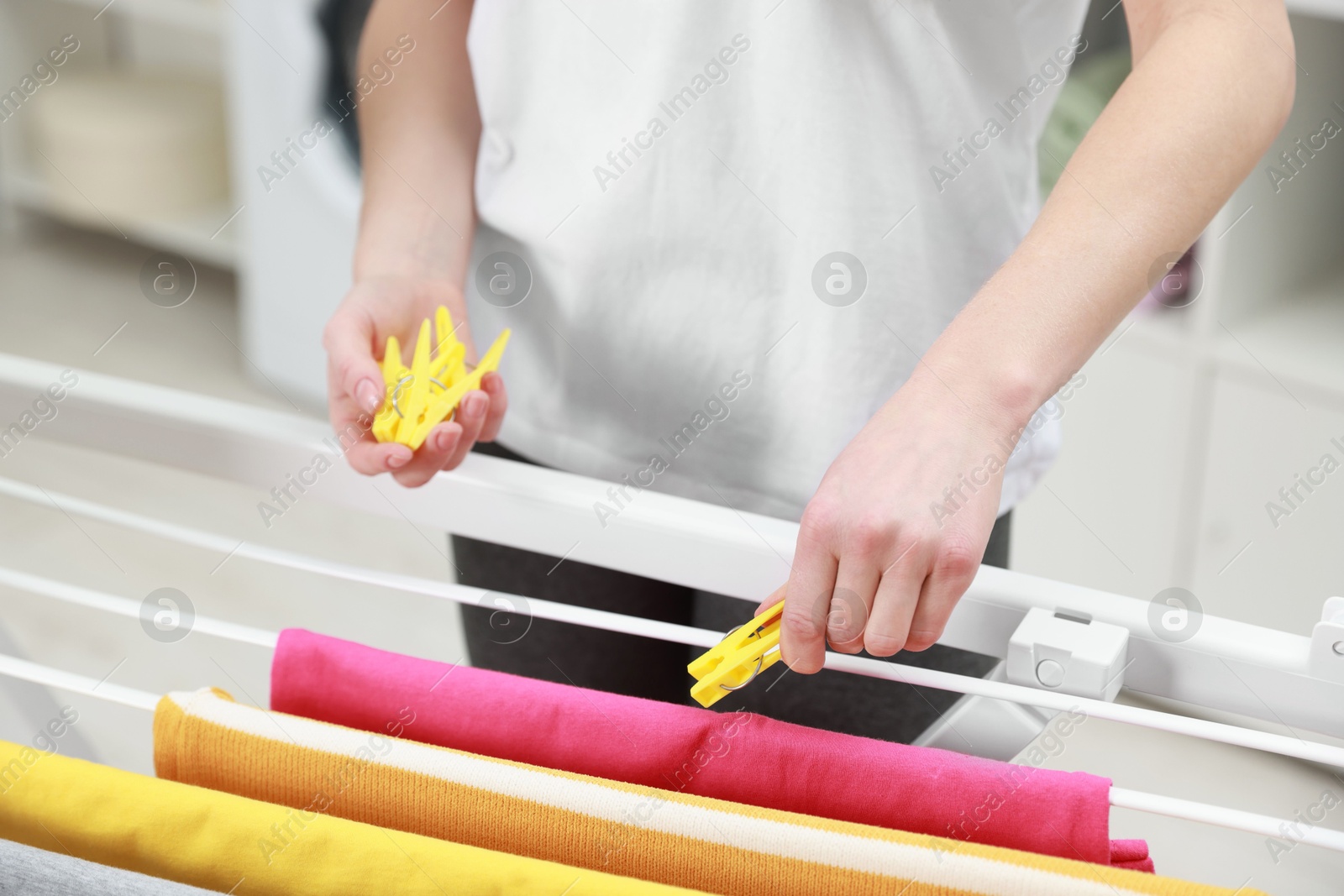 Photo of Woman hanging fresh clean laundry on drying rack at home, closeup