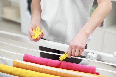 Photo of Woman hanging fresh clean laundry on drying rack at home, closeup