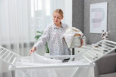 Photo of Beautiful woman hanging fresh clean laundry on drying rack at home