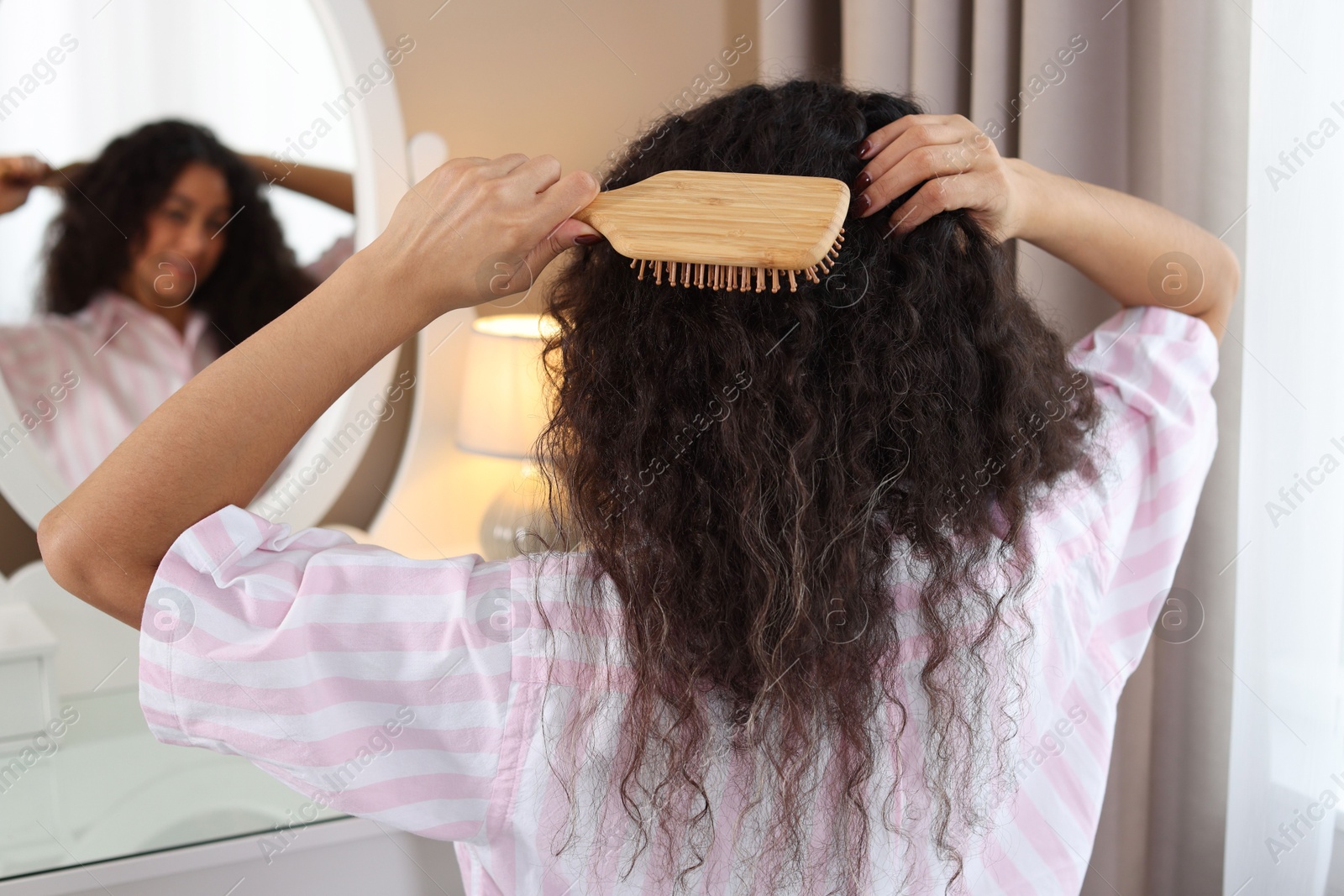 Photo of Woman brushing her curly hair near mirror at home, selective focus