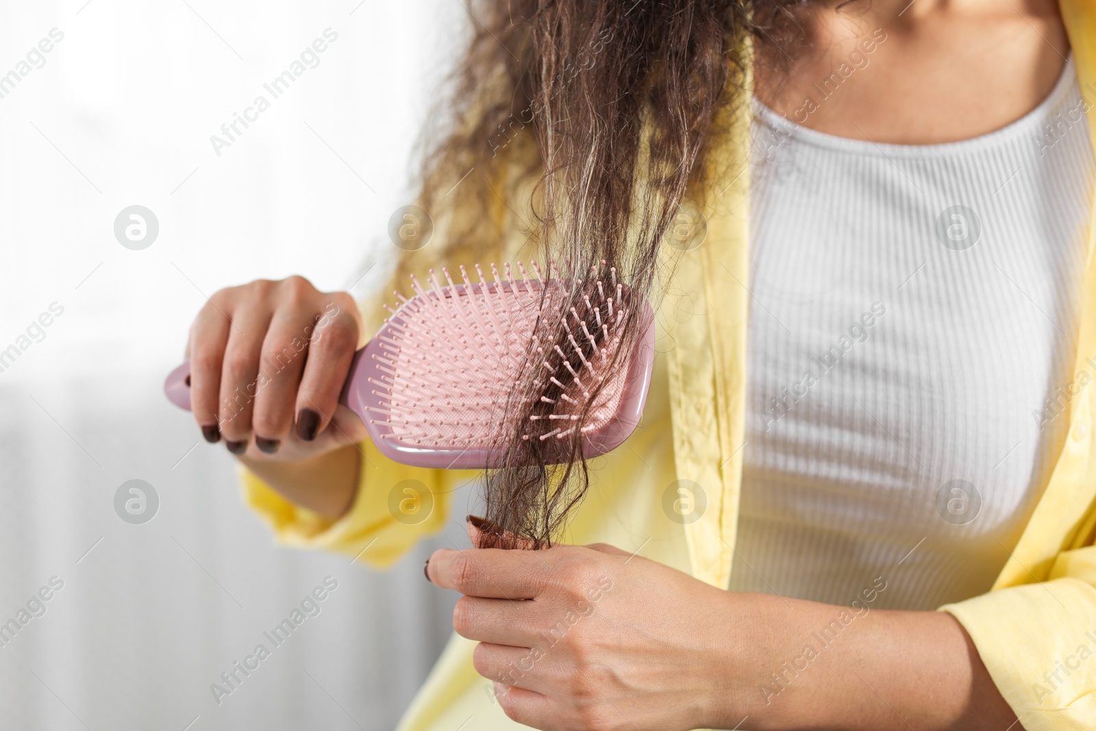 Photo of Woman brushing her curly hair indoors, closeup