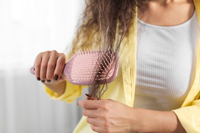 Photo of Woman brushing her curly hair indoors, closeup