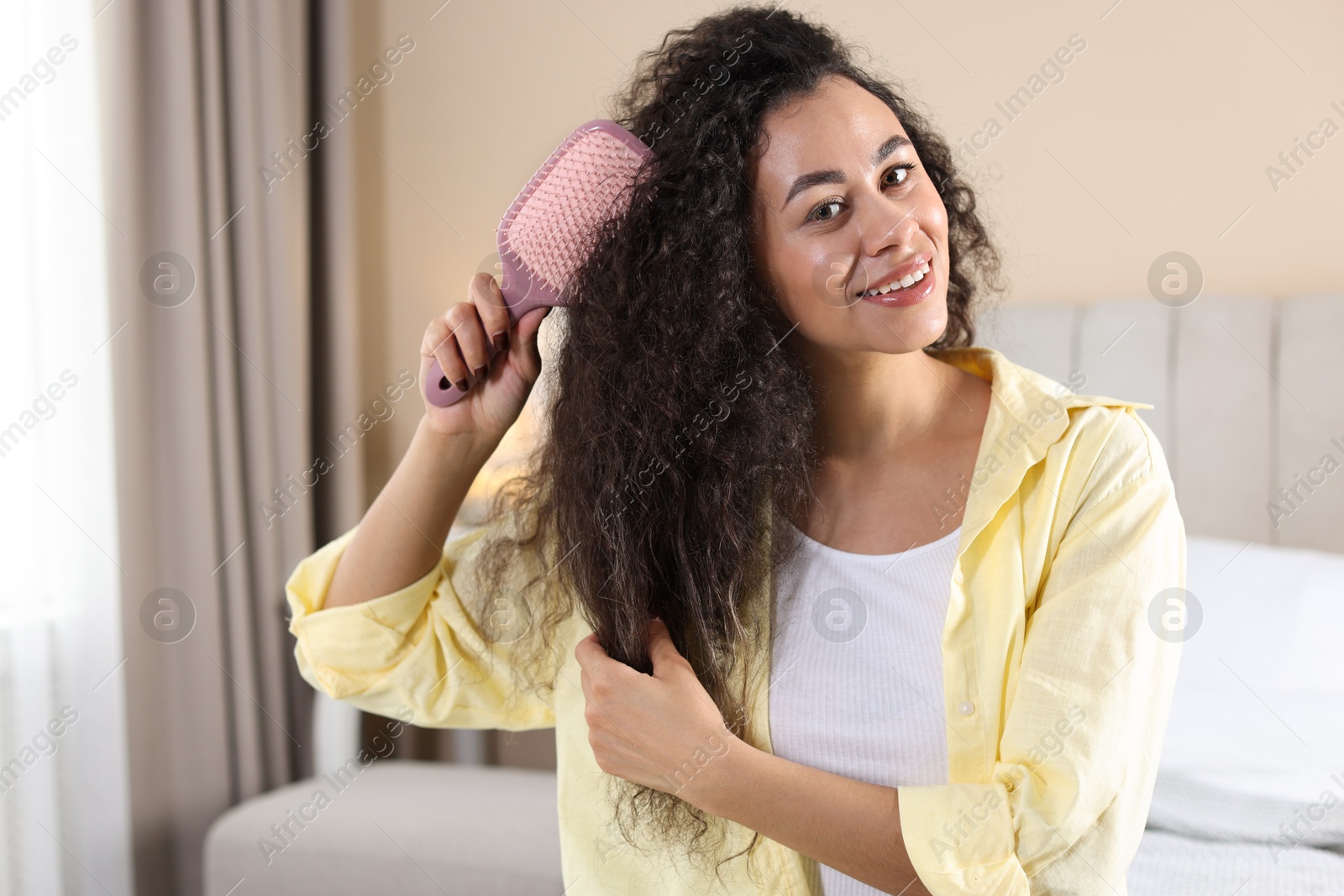 Photo of Smiling young woman brushing her curly hair at home