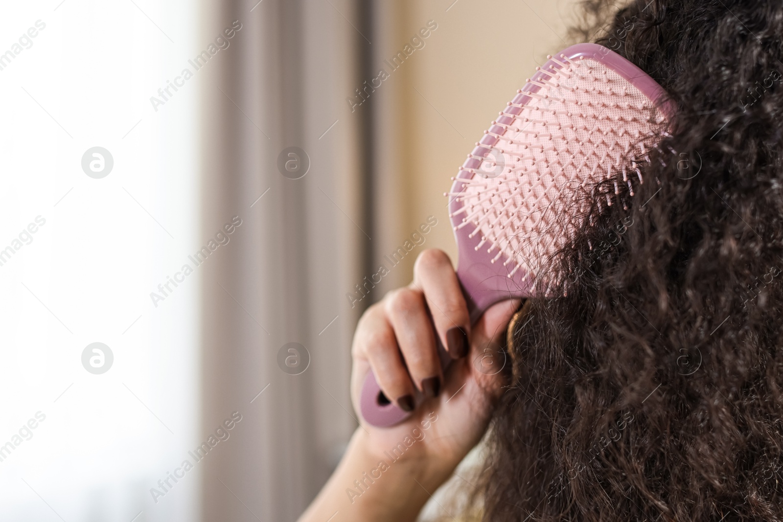 Photo of Woman brushing her curly hair indoors, closeup. Space for text