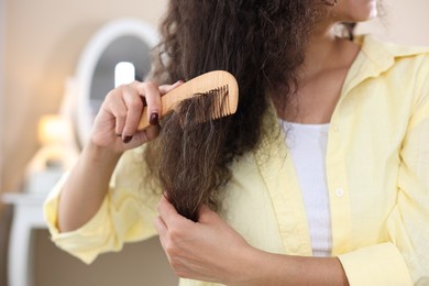 Photo of Woman brushing her curly hair with comb indoors, closeup