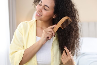 Photo of Smiling young woman brushing her curly hair with comb at home