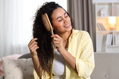 Photo of Smiling young woman brushing her curly hair at home