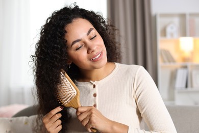 Photo of Smiling young woman brushing her curly hair at home