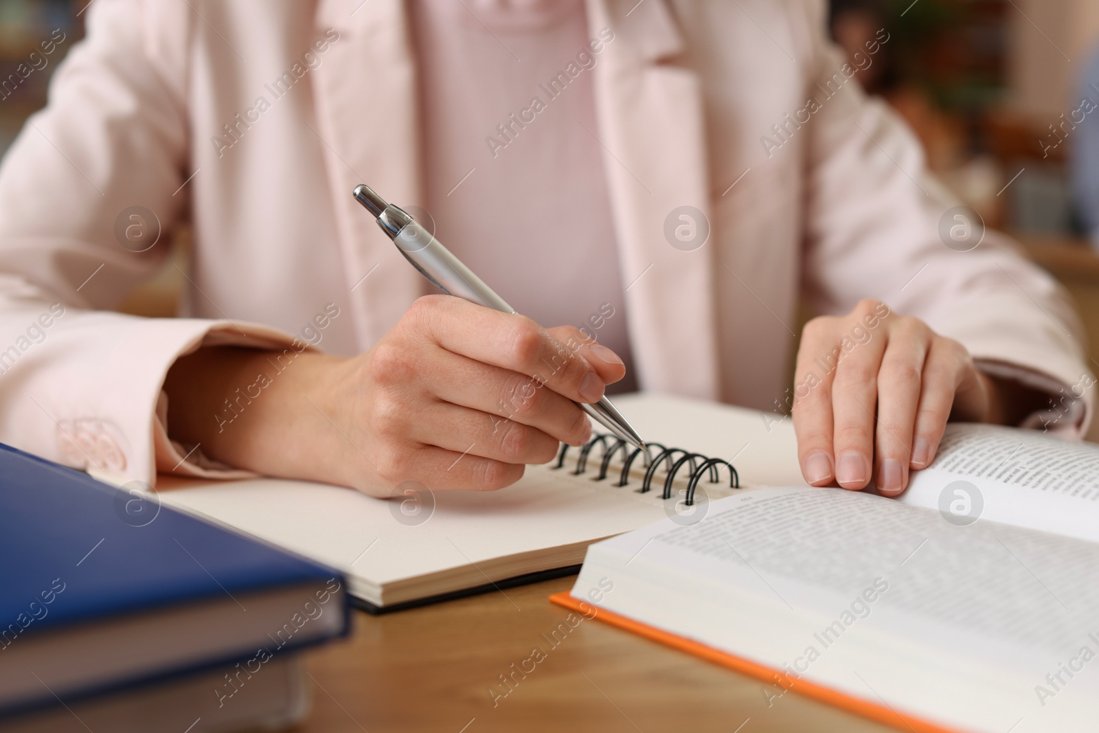 Photo of Woman reading book and taking notes at desk in library, closeup