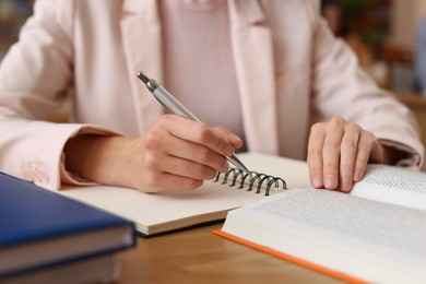 Photo of Woman reading book and taking notes at desk in library, closeup