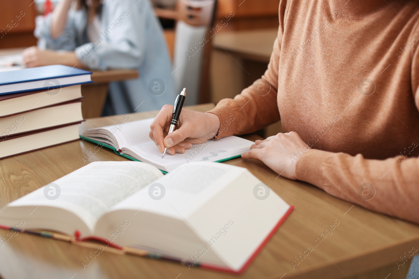 Photo of Woman reading book and taking notes at desk in library, closeup