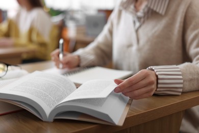 Photo of Woman reading book and taking notes at desk in library, closeup