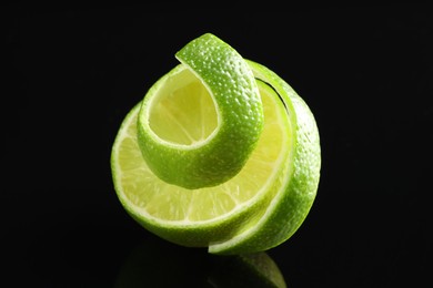 Photo of Fresh lime peel and half of fruit on black glass surface, closeup