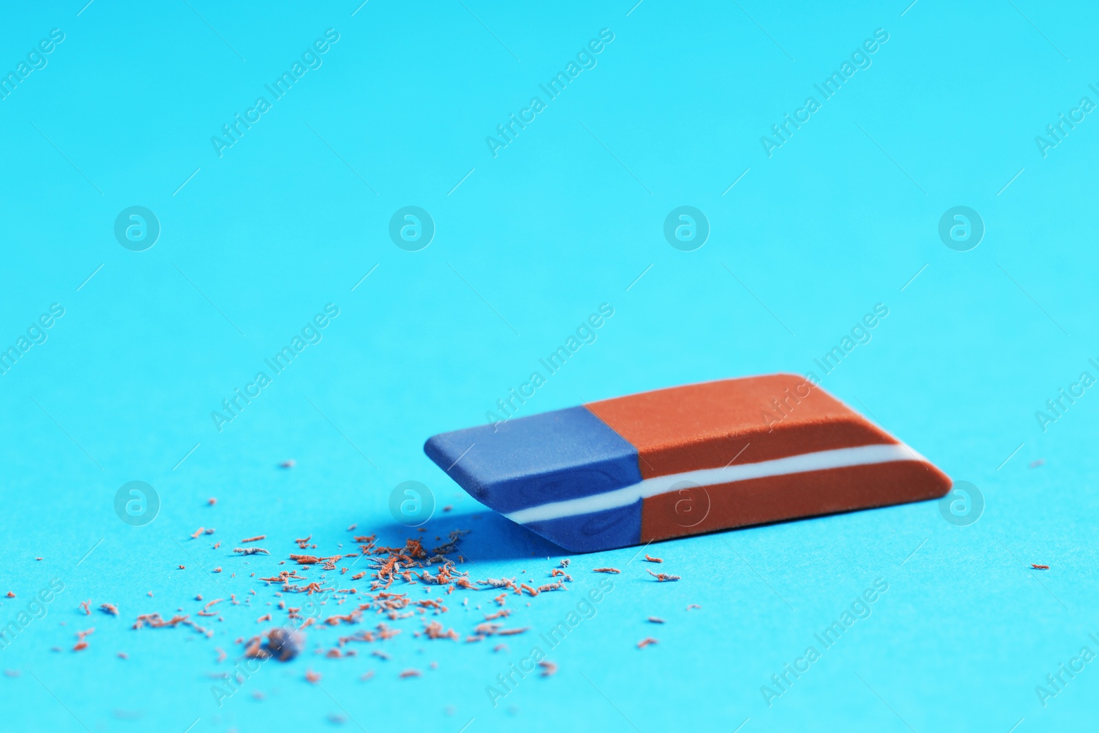 Photo of One eraser and scraps on light blue background, closeup