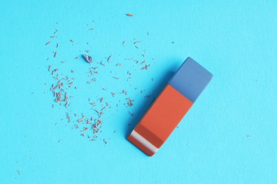 Photo of One eraser and scraps on light blue background, top view