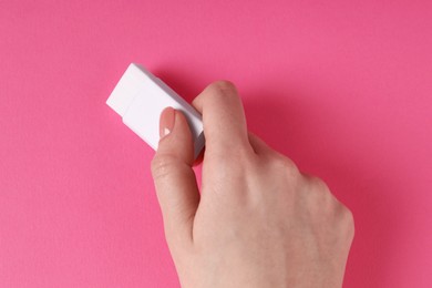 Photo of Woman using eraser on pink background, closeup