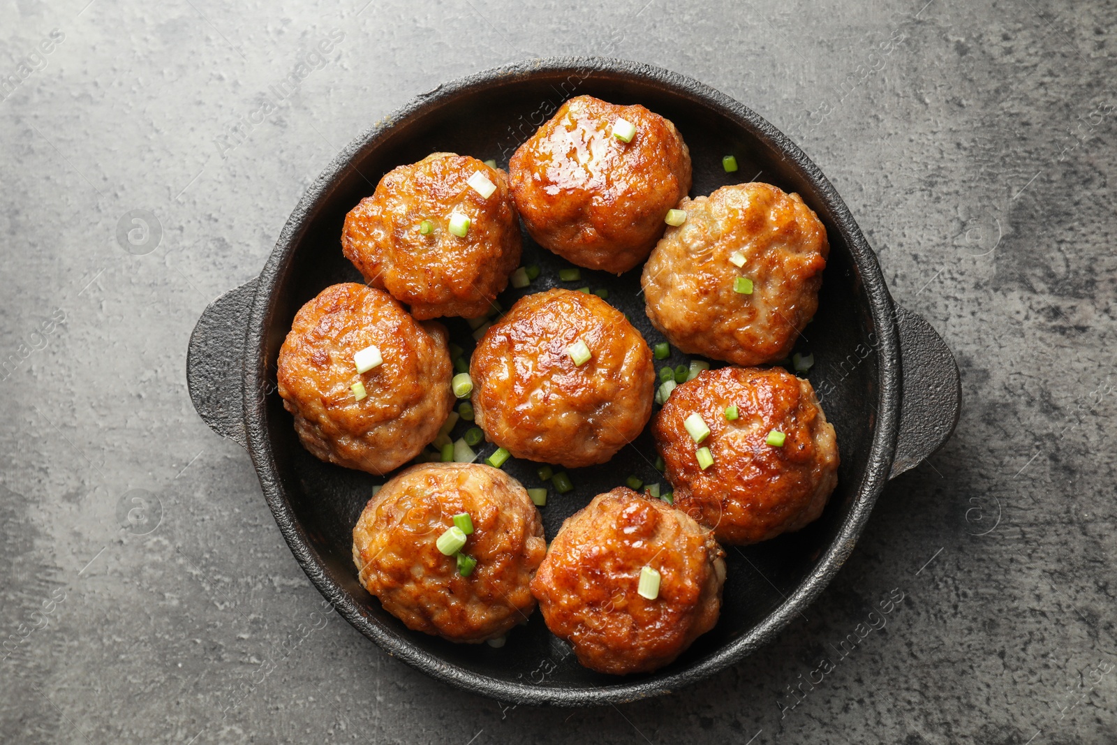 Photo of Tasty meatballs with green onion in baking dish on grey table, top view