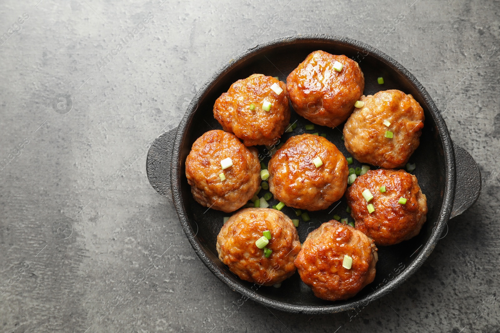 Photo of Tasty meatballs with green onion in baking dish on grey table, top view. Space for text