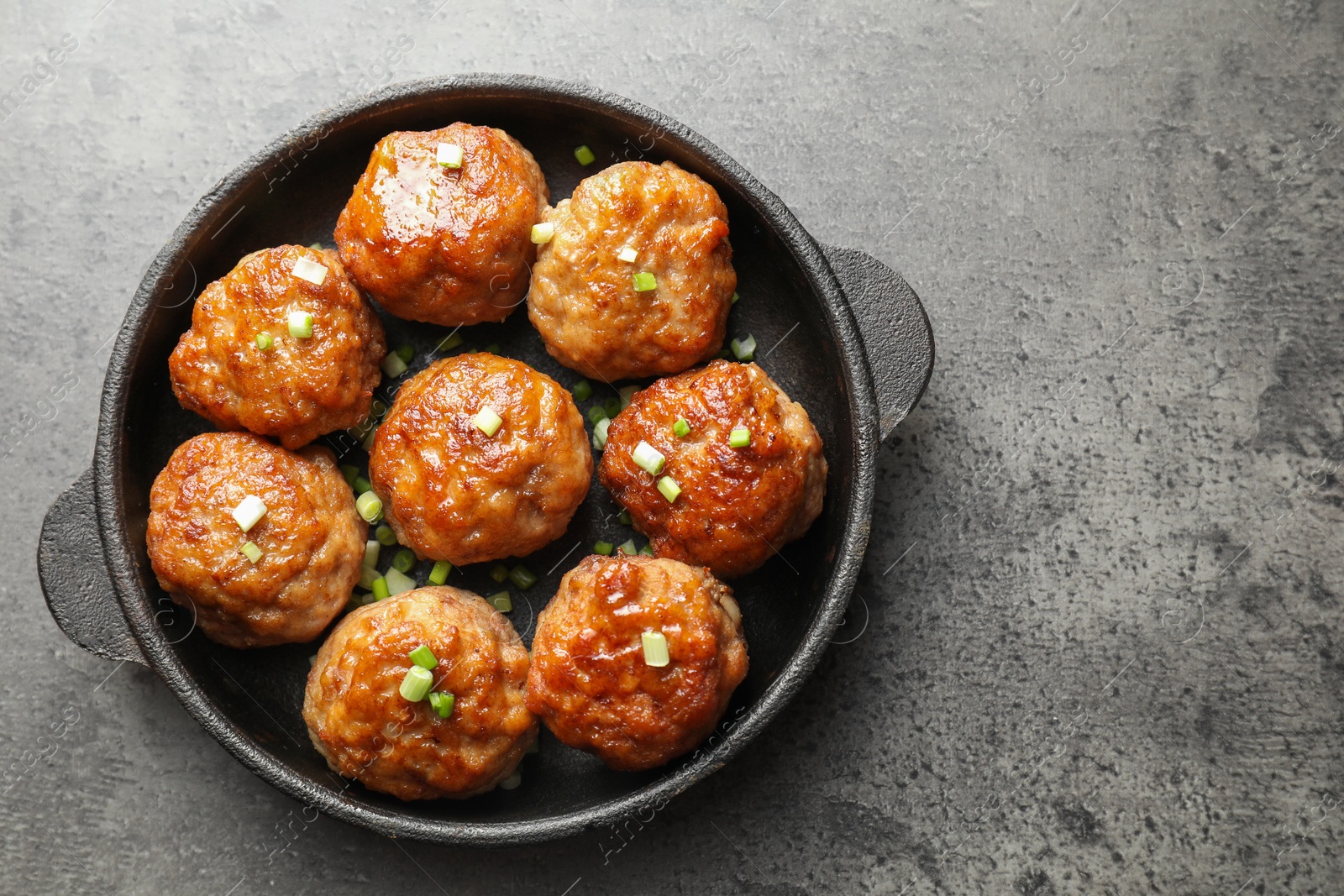 Photo of Tasty meatballs with green onion in baking dish on grey table, top view. Space for text