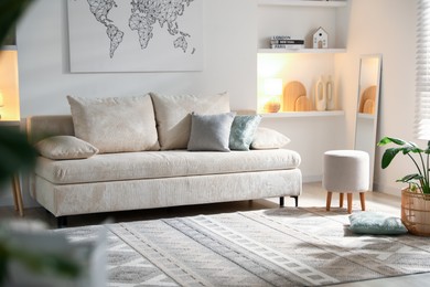 Photo of Comfortable sofa with pillows, pouf and houseplant in living room