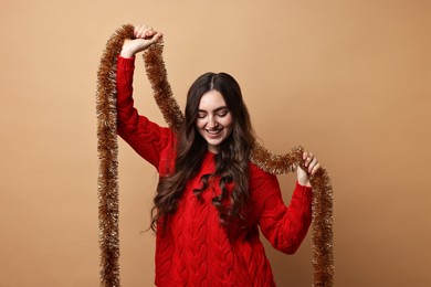 Photo of Happy young woman with tinsel on beige background