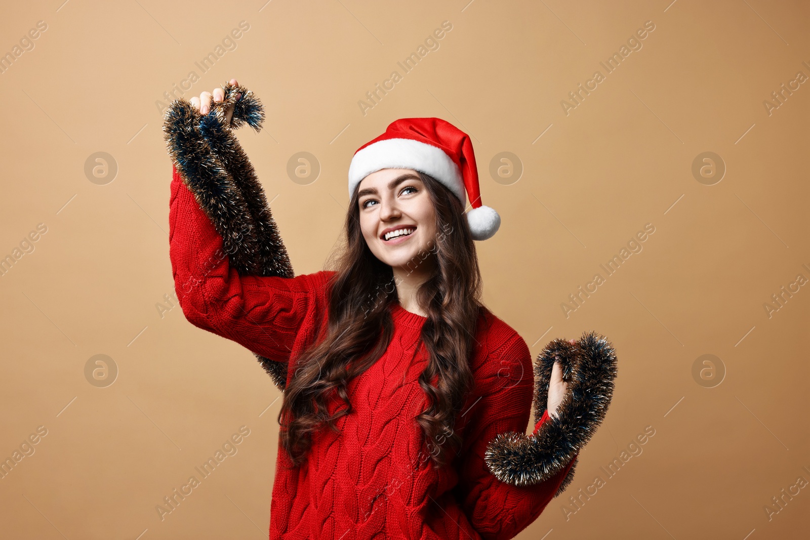 Photo of Happy young woman with tinsel and Santa hat on beige background