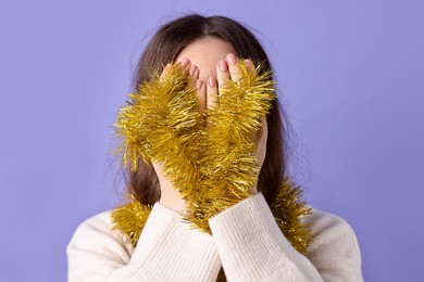 Photo of Woman covering eyes with yellow tinsel on purple background