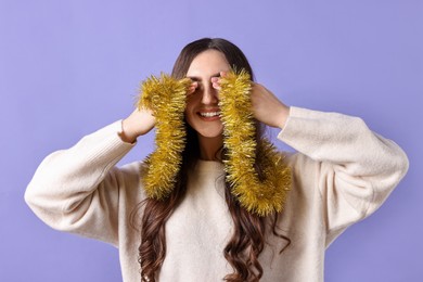 Photo of Happy young woman with yellow tinsel covering eyes on purple background