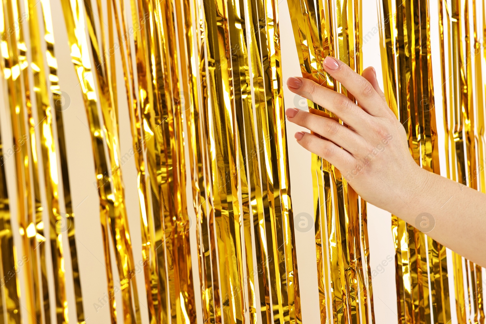 Photo of Woman near golden foil curtain against beige background, closeup