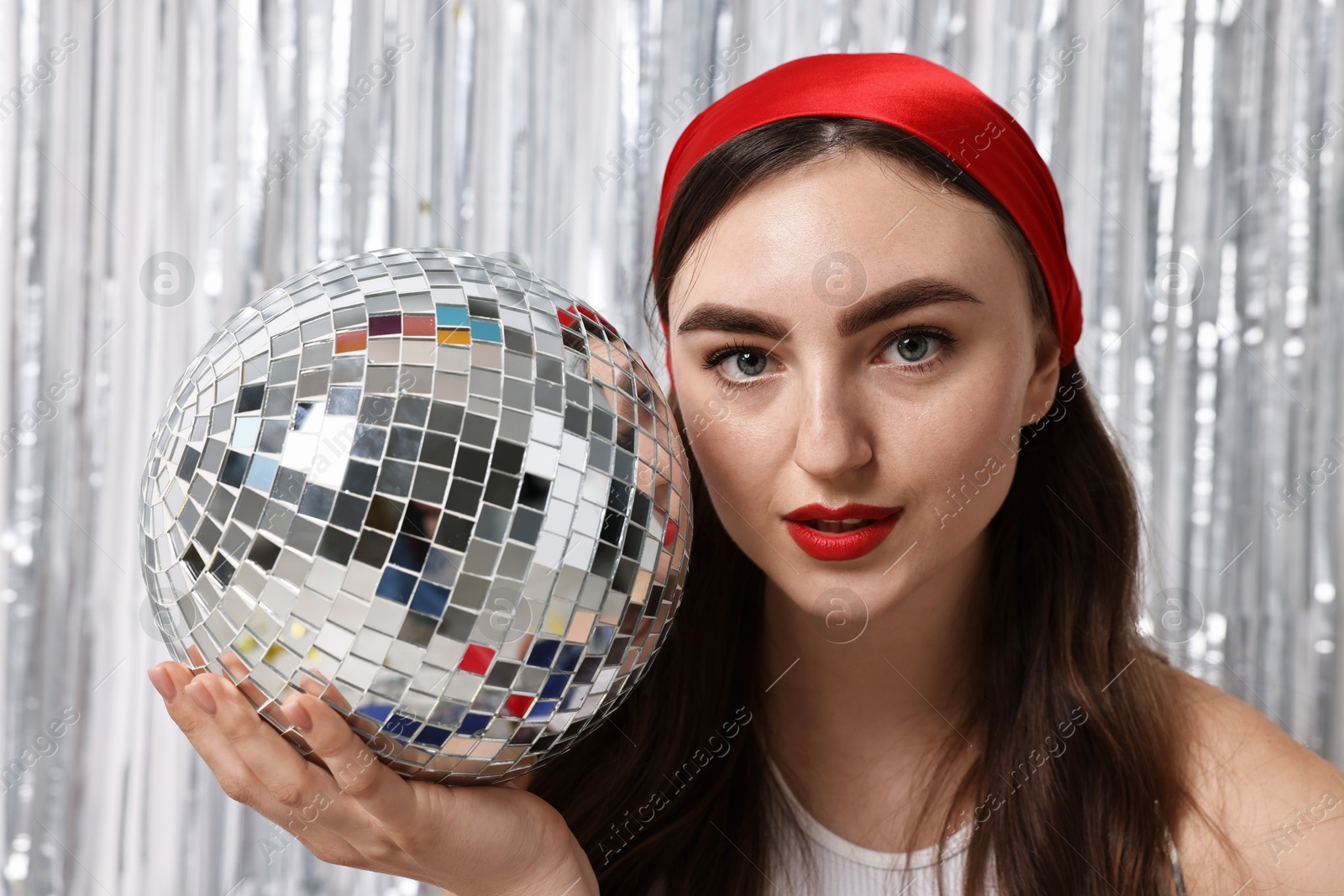 Photo of Portrait of beautiful young woman with disco ball against silver foil curtain