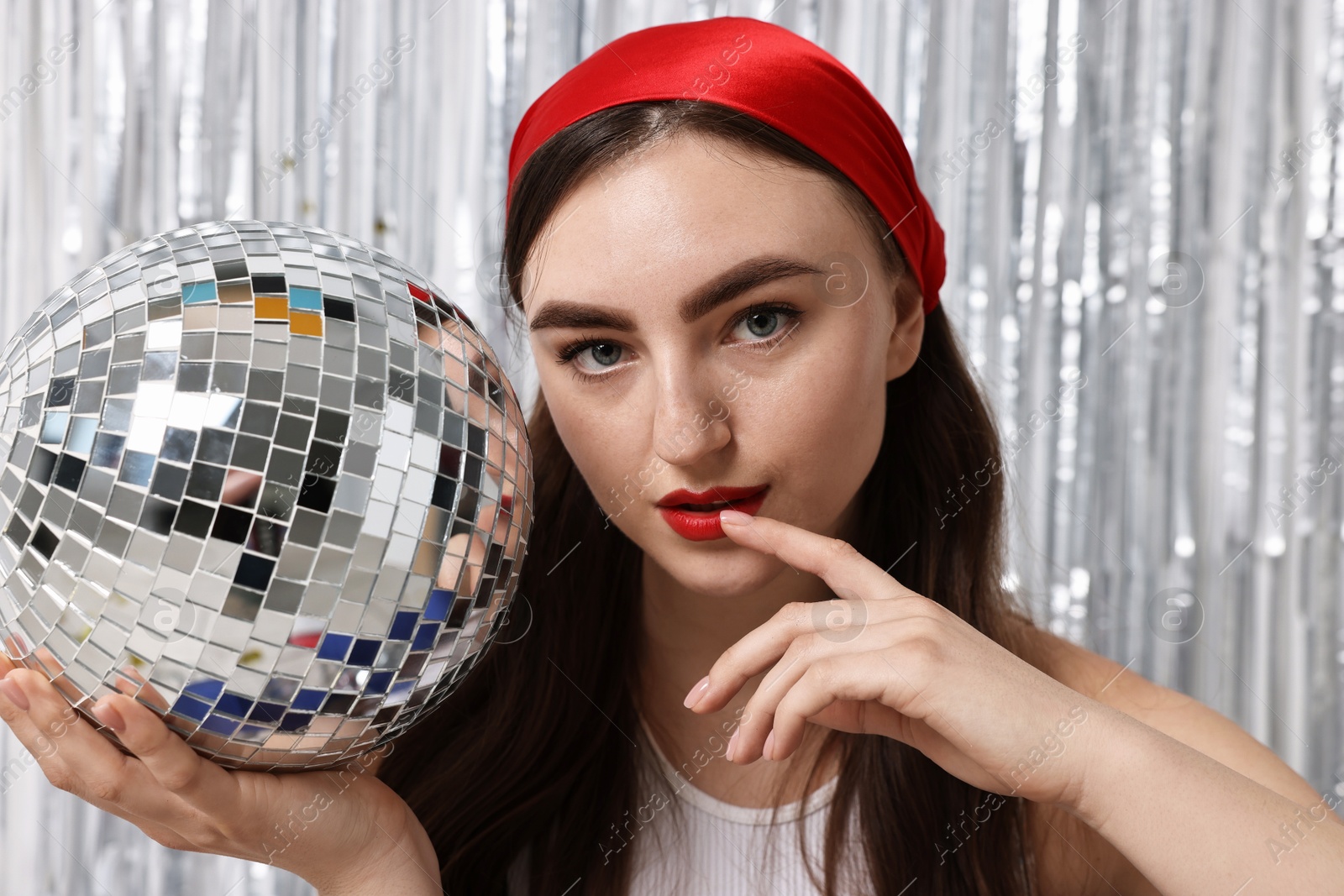 Photo of Portrait of beautiful young woman with disco ball against silver foil curtain