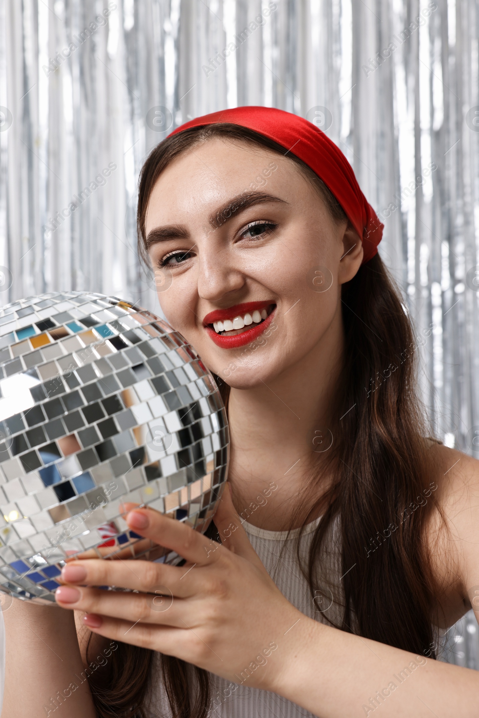 Photo of Portrait of beautiful young woman with disco ball against silver foil curtain