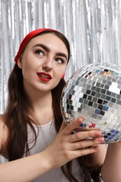 Photo of Portrait of beautiful young woman with disco ball against silver foil curtain