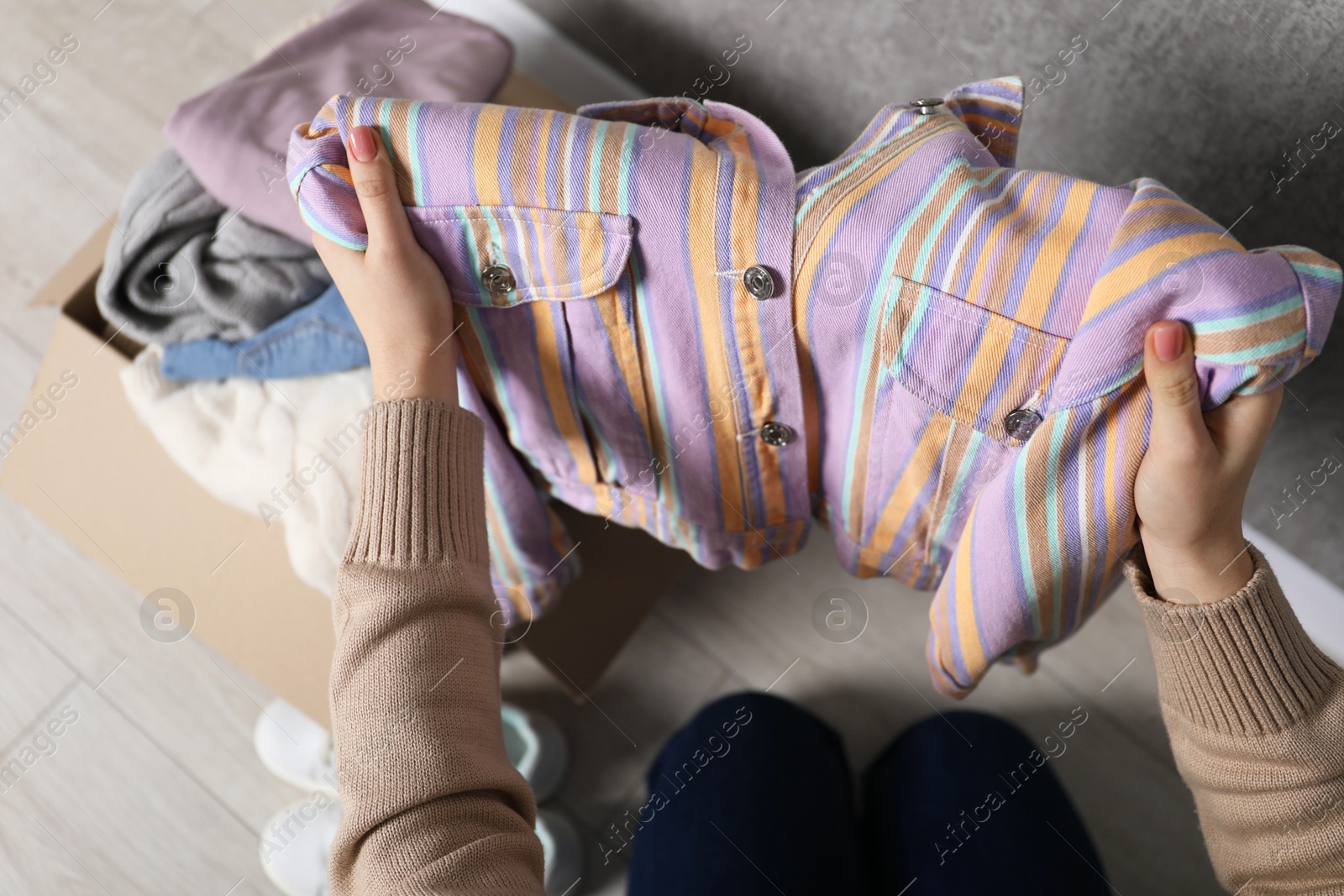 Photo of Woman stacking used clothes into box indoors, above view