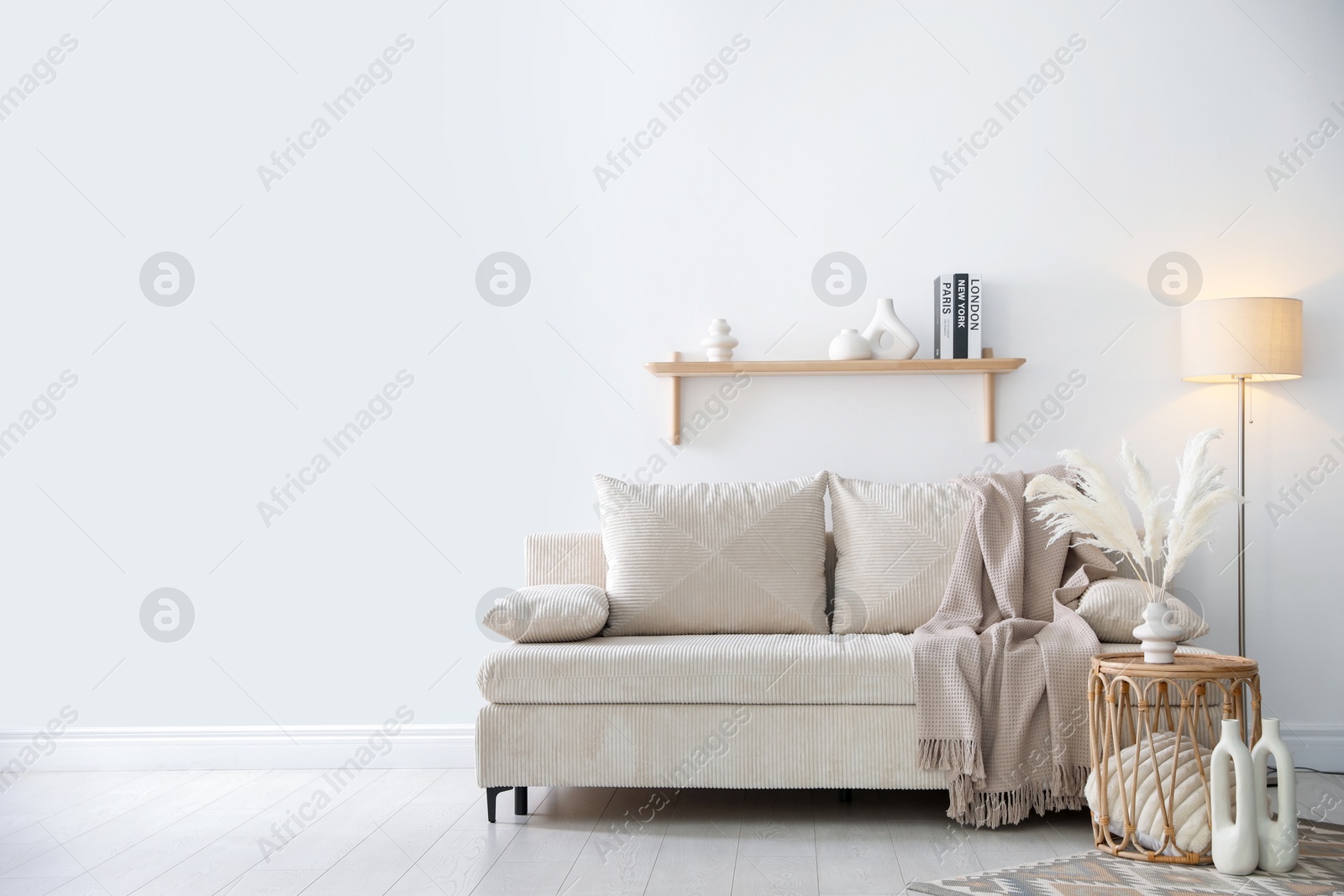 Photo of Comfortable sofa with pillows, blanket, lamp and different decor near white wall indoors, space for text