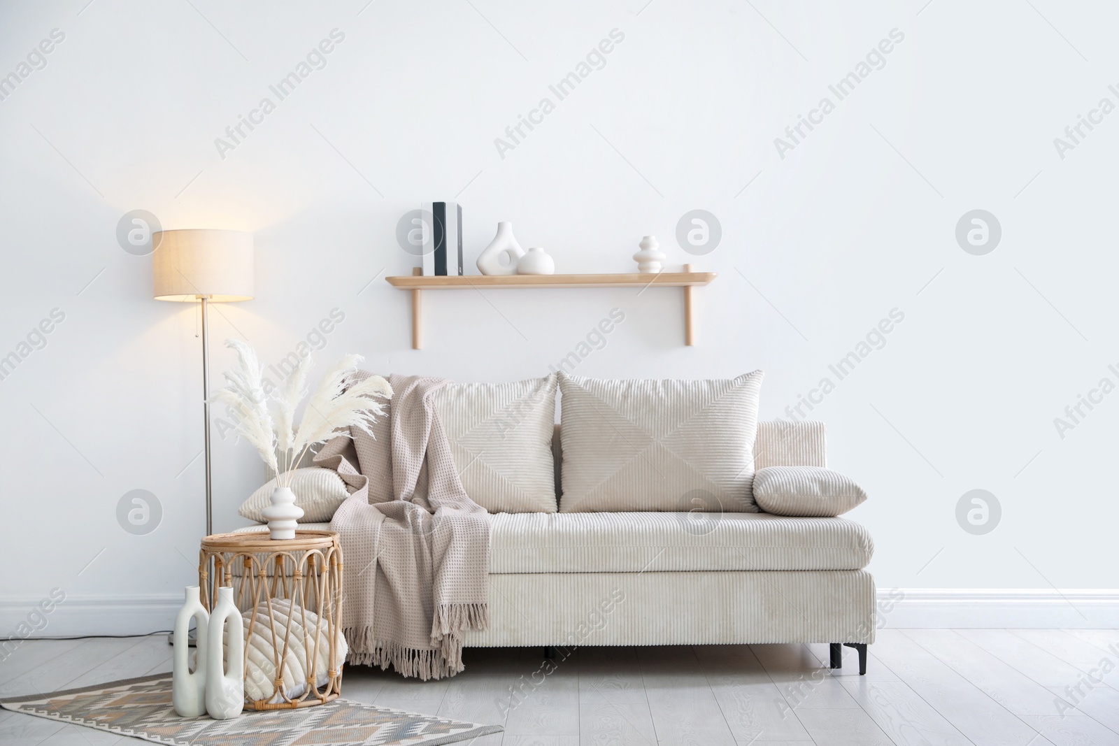 Photo of Comfortable sofa with pillows, blanket, lamp and different decor near white wall indoors