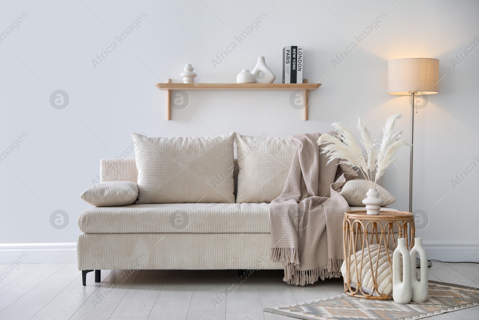 Photo of Comfortable sofa with pillows, blanket, lamp and different decor near white wall indoors