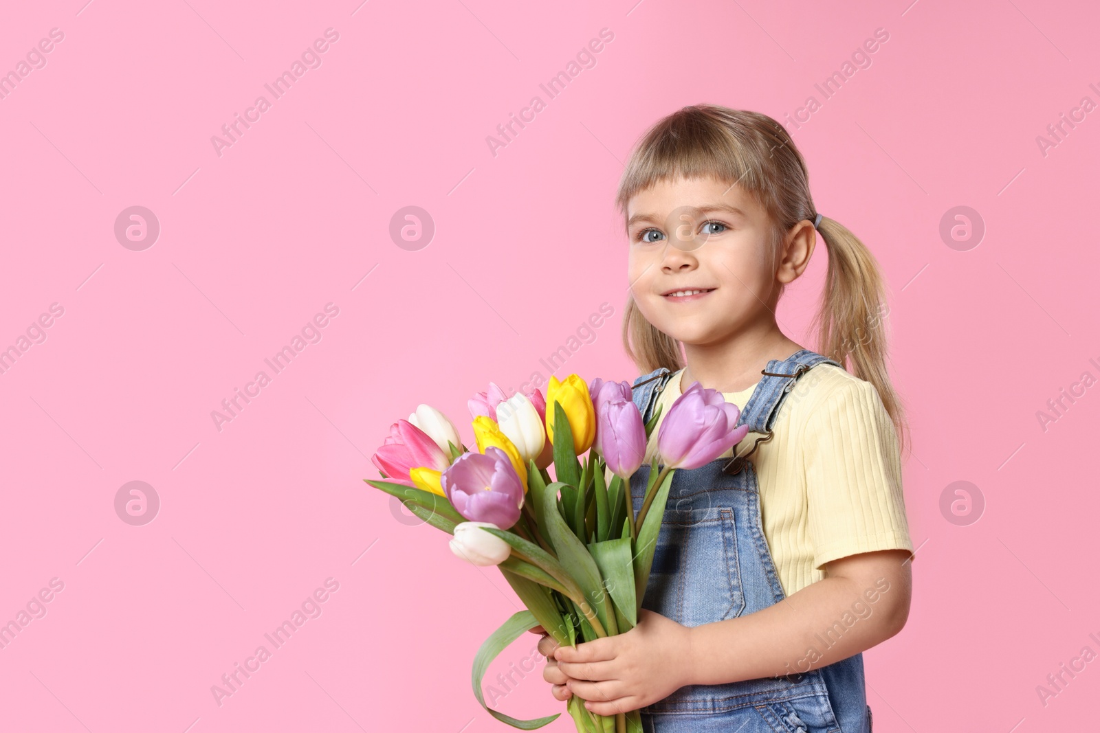 Photo of Smiling little girl with bouquet of tulips on pink background. Space for text