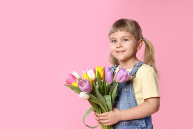 Photo of Smiling little girl with bouquet of tulips on pink background. Space for text