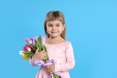 Photo of Cute little girl with bouquet of tulips on light blue background. Space for text