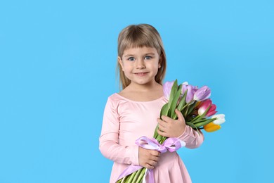 Photo of Smiling little girl with bouquet of tulips on light blue background. Space for text