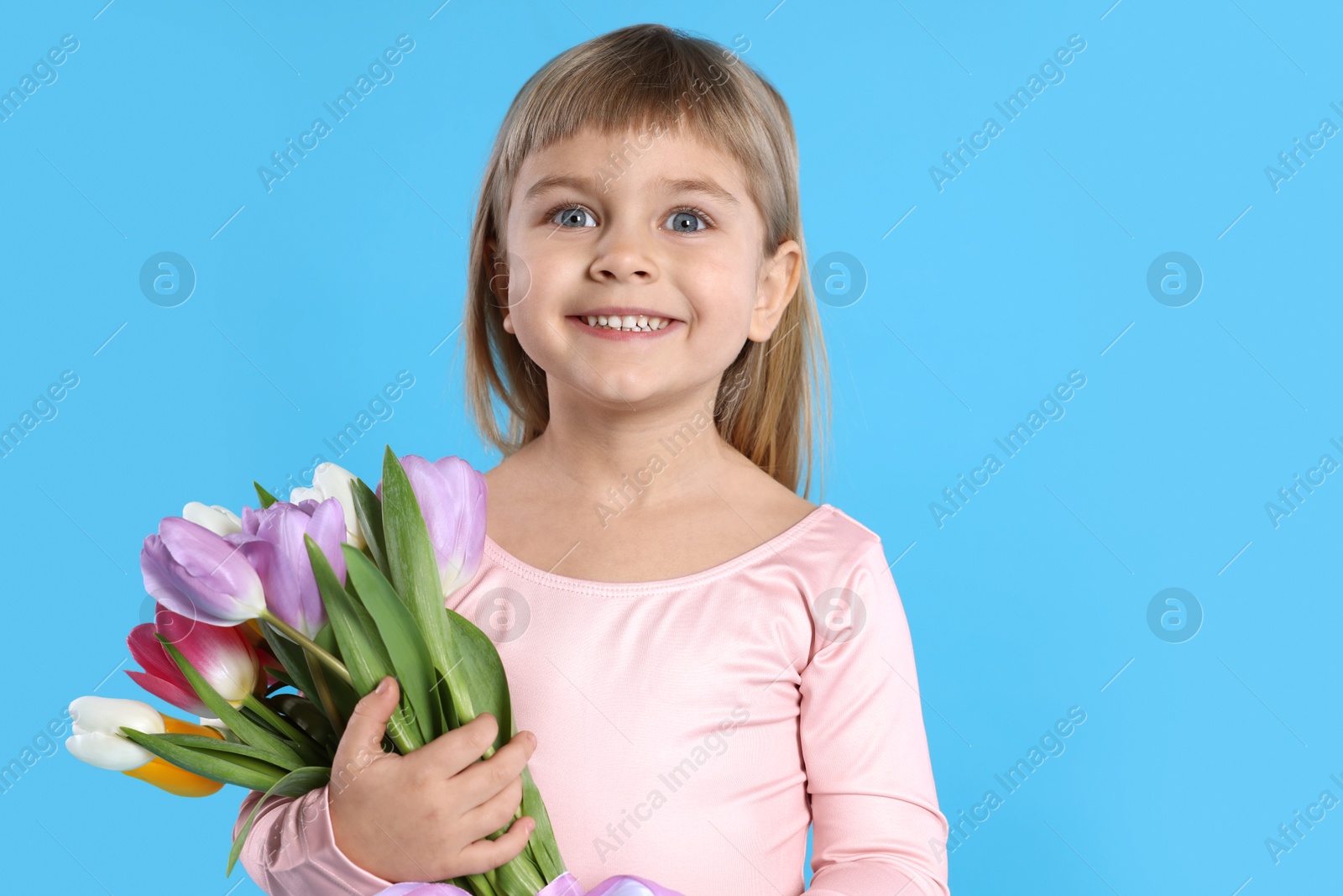 Photo of Smiling little girl with bouquet of tulips on light blue background