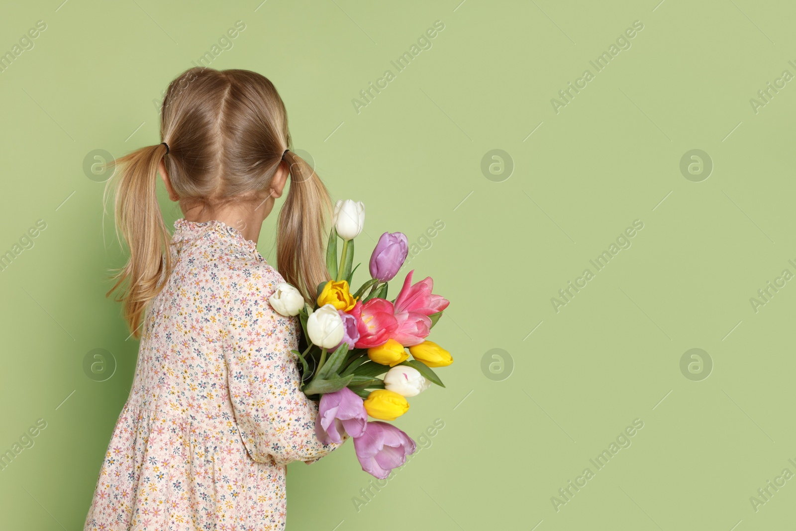 Photo of Little girl with bouquet of tulips on green background, back view. Space for text