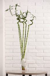 Photo of Decorative green bamboo stems in vase on table near white brick wall