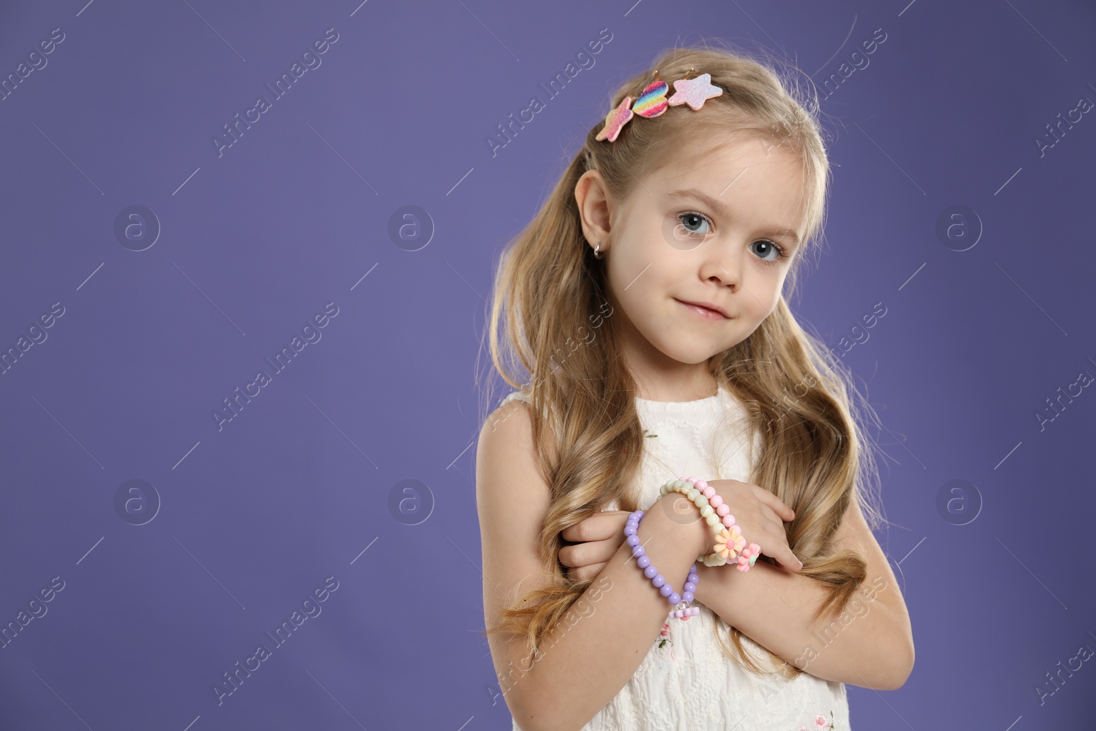 Photo of Cute little girl with beautiful hair clips on violet background. Space for text