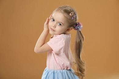 Photo of Cute little girl wearing beautiful hair accessories on light brown background